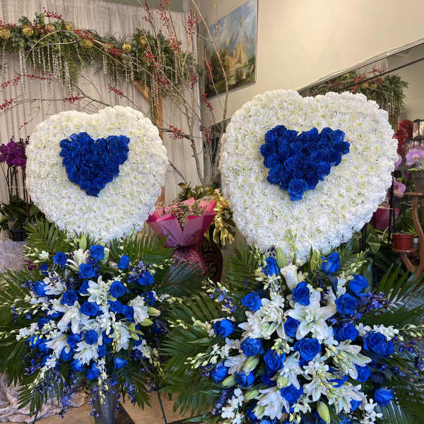 Two large heart-shaped floral tributes with blue roses and white flowers
