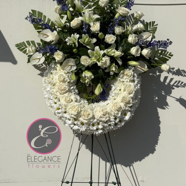 Standing white floral wreath with roses, lilies, and blue accents on an easel