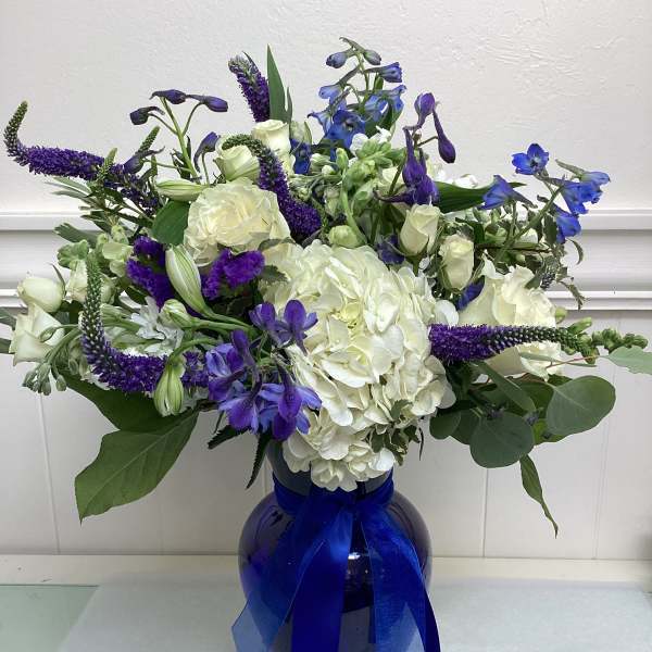 White and blue floral arrangement in a dark vase with a blue ribbon