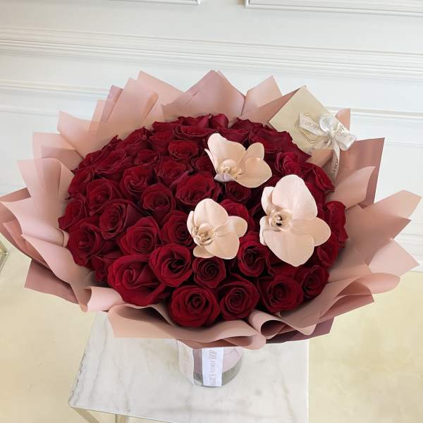 Bouquet of red roses with pale pink orchid accents in pink wrap