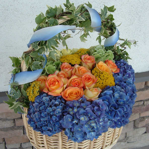 Basket arrangement of orange roses and blue hydrangeas with ivy and ribbon