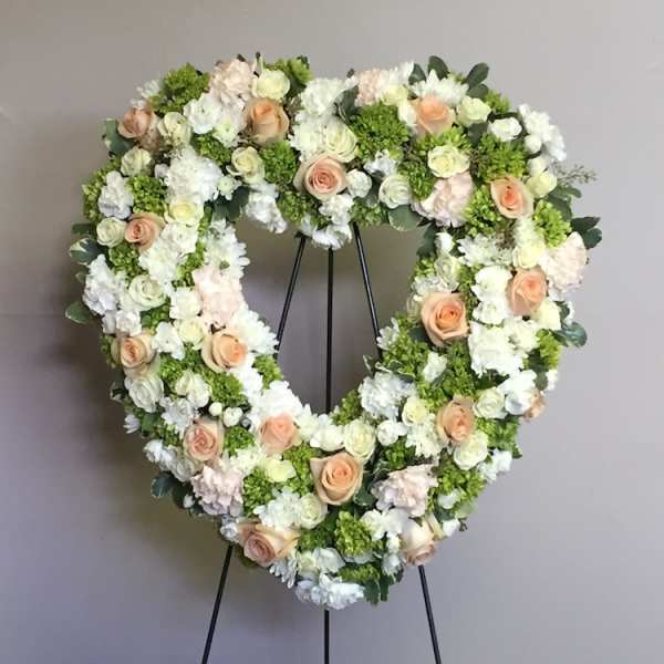 Heart-shaped floral wreath on a stand with white and peach flowers