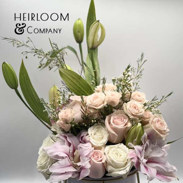 Blush roses and pink lilies arranged in a white vase with tall buds