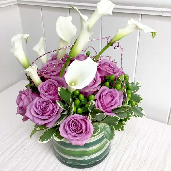 Purple roses and white calla lilies in a striped ceramic vase