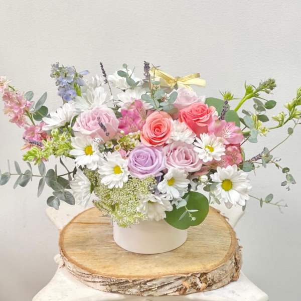 Pastel bouquet of roses and daisies in a white container