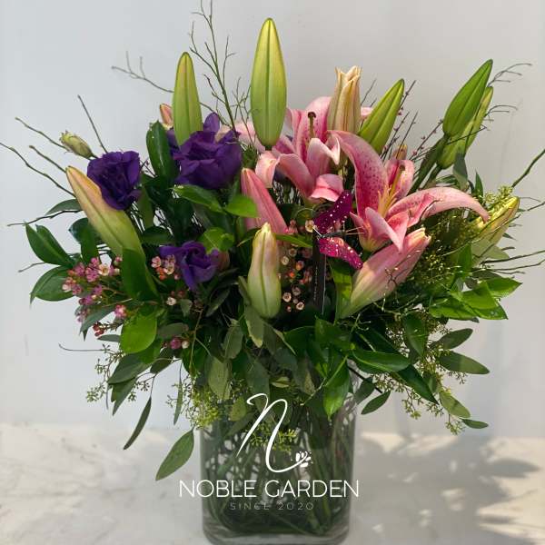 Pink lilies and purple blooms arranged in a glass vase