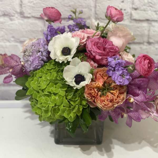 Mixed bouquet in a square glass vase with pink, purple, white, and green blooms