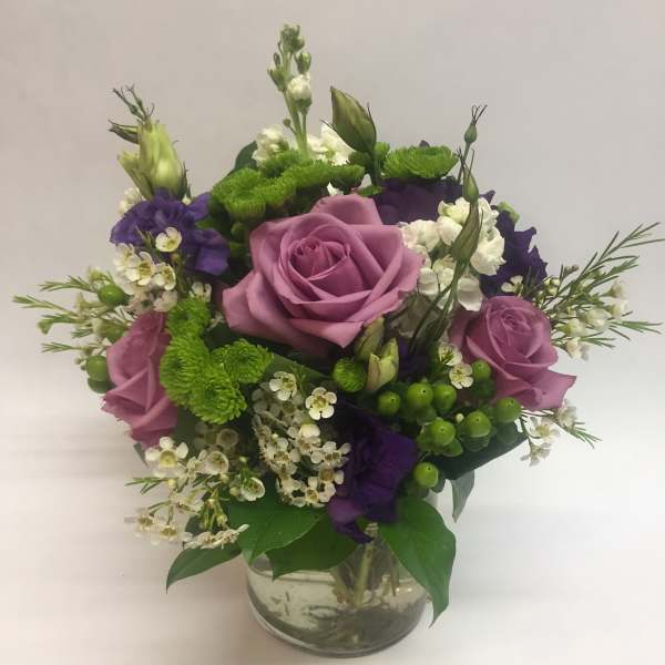 Mixed bouquet of pink roses, purple blooms, and white flowers in a glass vase