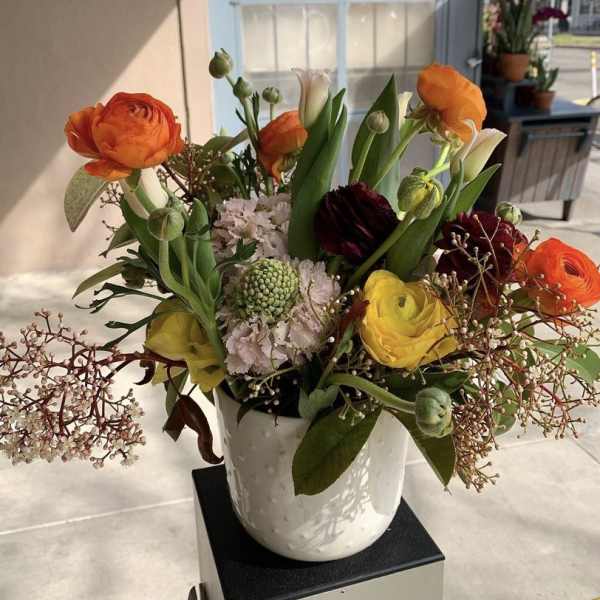 Mixed bouquet of orange, yellow, and burgundy flowers in a white vase