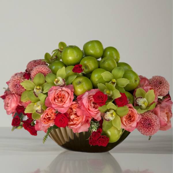 Pink and red floral arrangement with green apples in a low vase