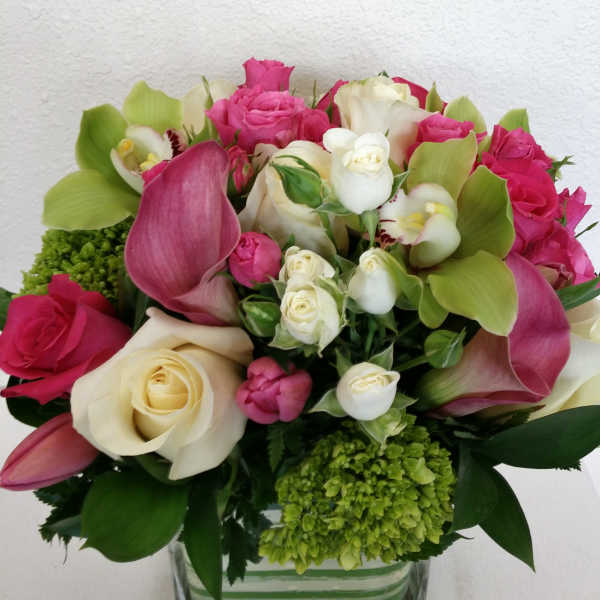Pink and white roses with green orchids in a glass vase