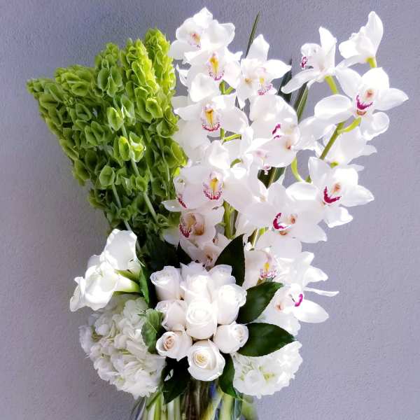 White orchids and roses arranged in a glass vase with green blooms
