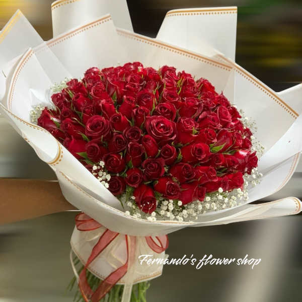 Large bouquet of red roses with white filler flowers wrapped in white paper and tied with a ribbon