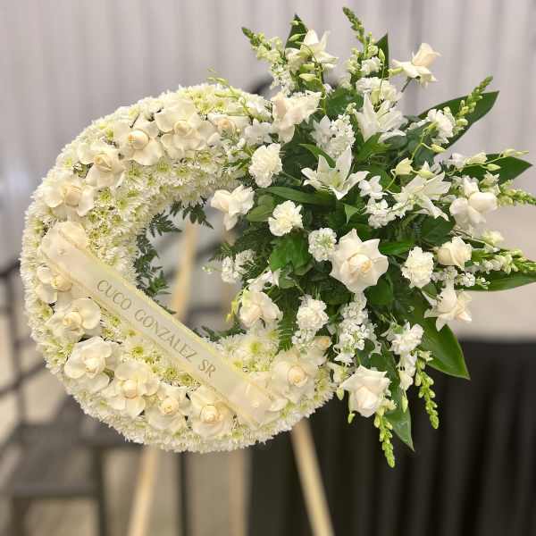 Standing white funeral wreath with roses and lilies on an easel with name ribbon