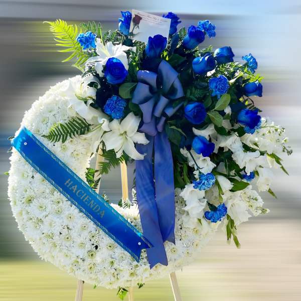 Standing white sympathy wreath with blue roses and ribbon on an easel