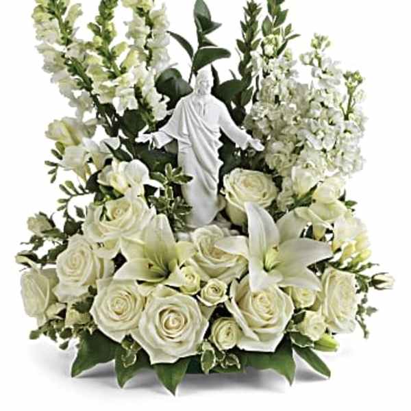 All-white arrangement of roses, lilies, and snapdragons surrounding a white Jesus figurine