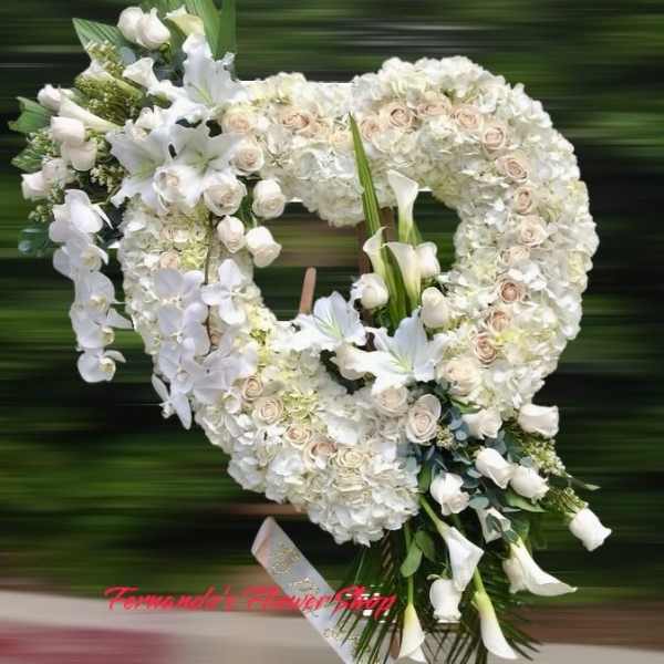 Large white heart-shaped standing wreath with roses, lilies, orchids, and calla lilies