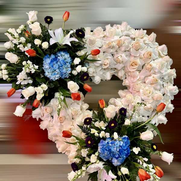 Heart-shaped standing spray of white roses with blue hydrangea clusters and orange tulips.