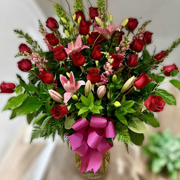 Tall arrangement of red roses and pink lilies in a glass vase with a bright pink bow