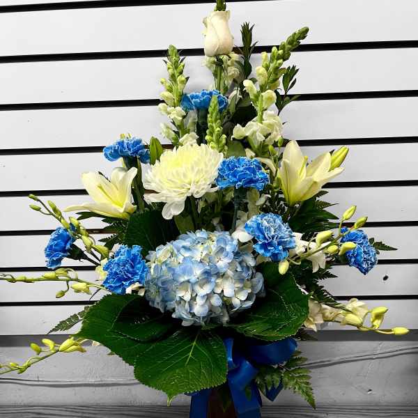 Tall blue and white flower arrangement with lilies, carnations, and hydrangea in a vase with a blue ribbon