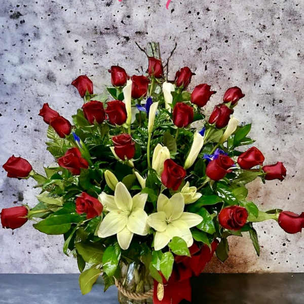 Large arrangement of red roses and white lilies with greenery in a clear glass vase tied with rope and a red bow