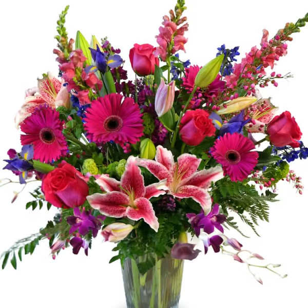 Tall mixed bouquet of pink lilies, roses, gerbera daisies and purple flowers in a clear glass vase