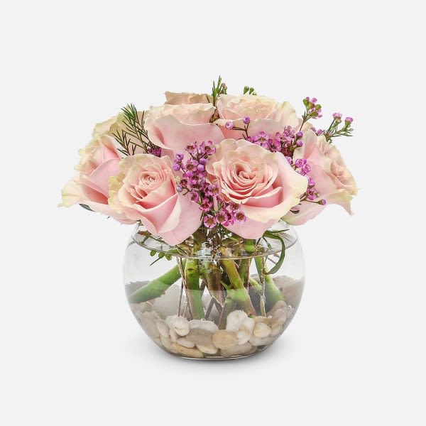 Pink roses arranged in a round glass vase with pebbles