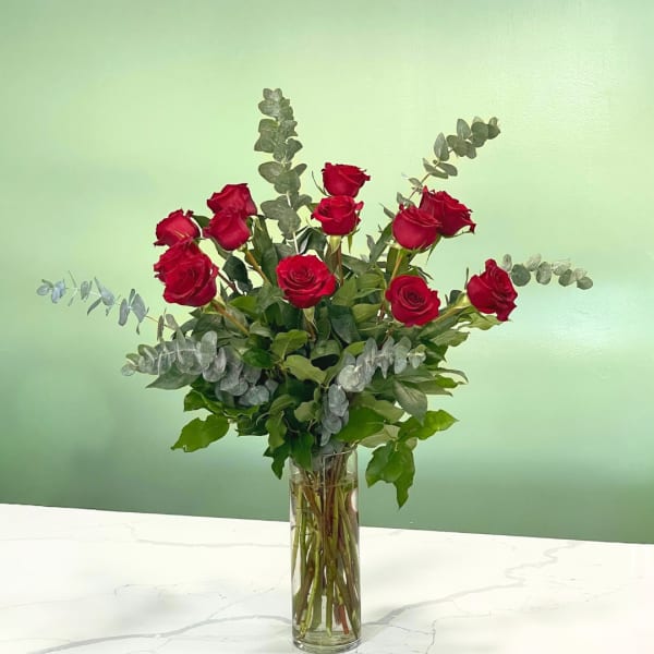Red roses arranged in a tall glass vase with eucalyptus