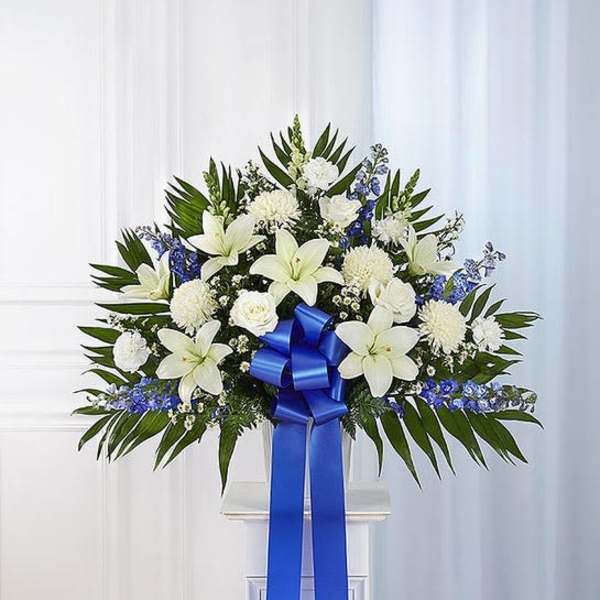 White lilies and blue flowers arranged with a large blue ribbon