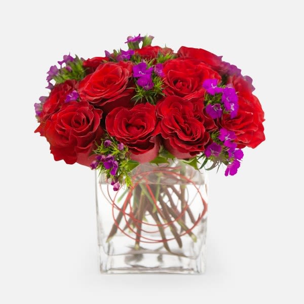 Red roses with purple accent flowers in a clear glass vase