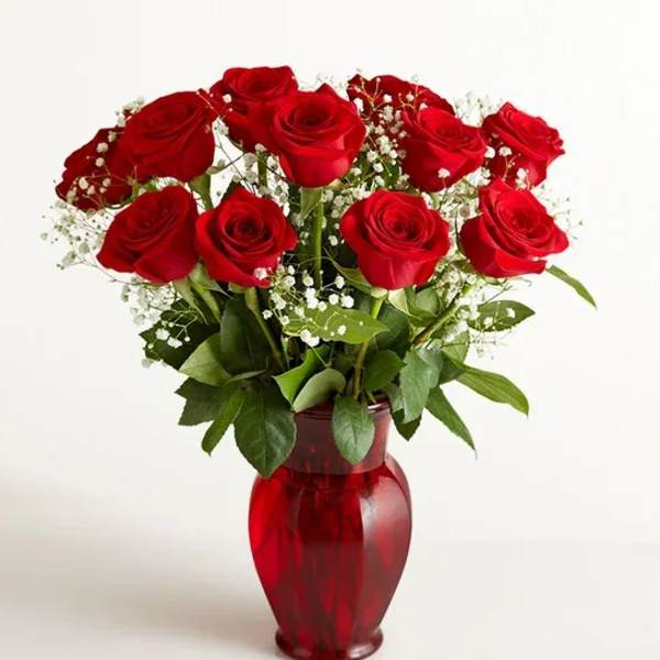 Red roses arranged in a red glass vase with baby's breath