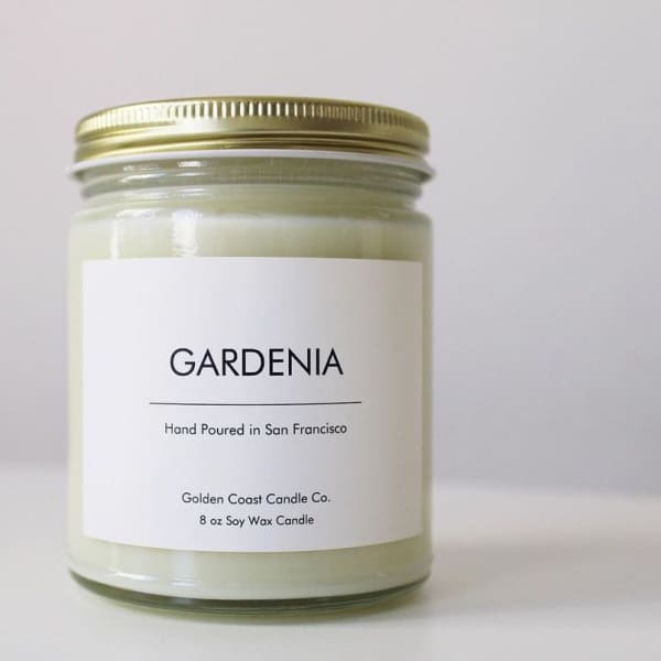 A gardenia-scented candle in a glass jar with a gold lid