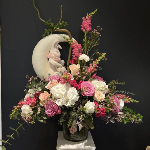 Pink and white floral arrangement with a rabbit figurine in a glass vase