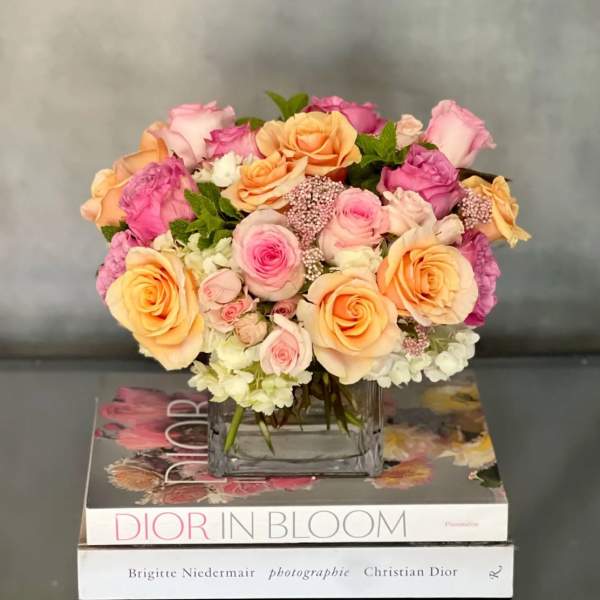 Low arrangement of peach and pink roses in a glass vase set on fashion books
