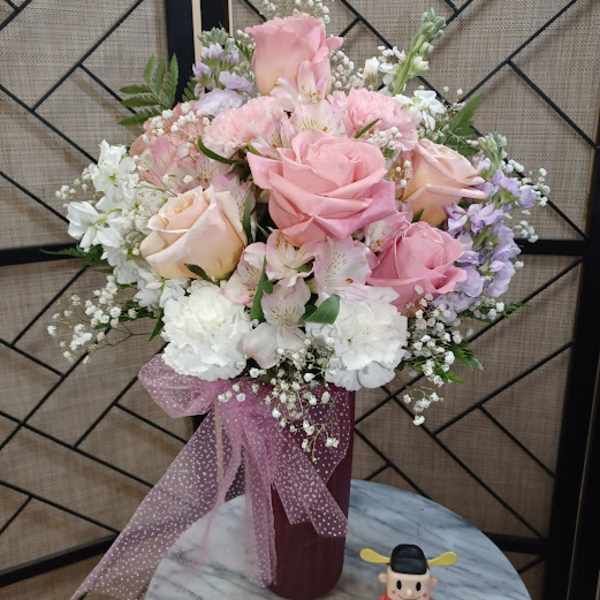 Pink and white rose bouquet in a burgundy vase with a pink ribbon