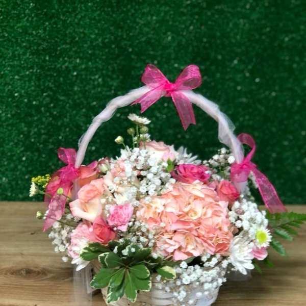 White basket of pink and white flowers with baby’s breath and pink bows on the handle