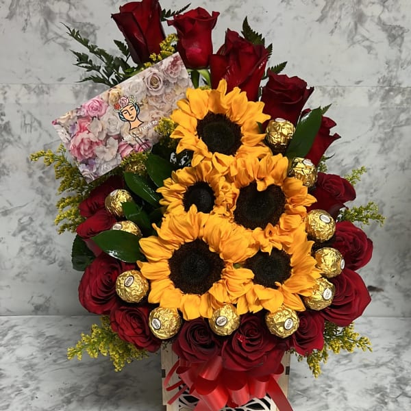 Arrangement of yellow sunflowers and red roses with gold-wrapped chocolates in a wooden box with a red bow and card.