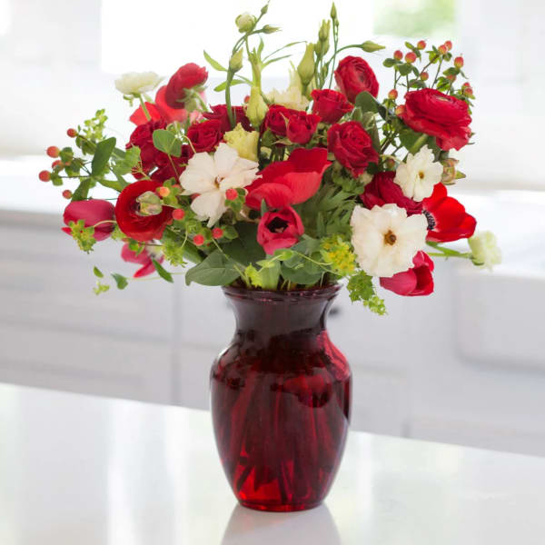 Red and white mixed flower arrangement with berries in a red glass vase on a white countertop