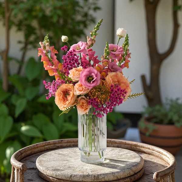 Tall mixed bouquet of pink lisianthus, peach roses, and magenta blooms in a clear glass vase