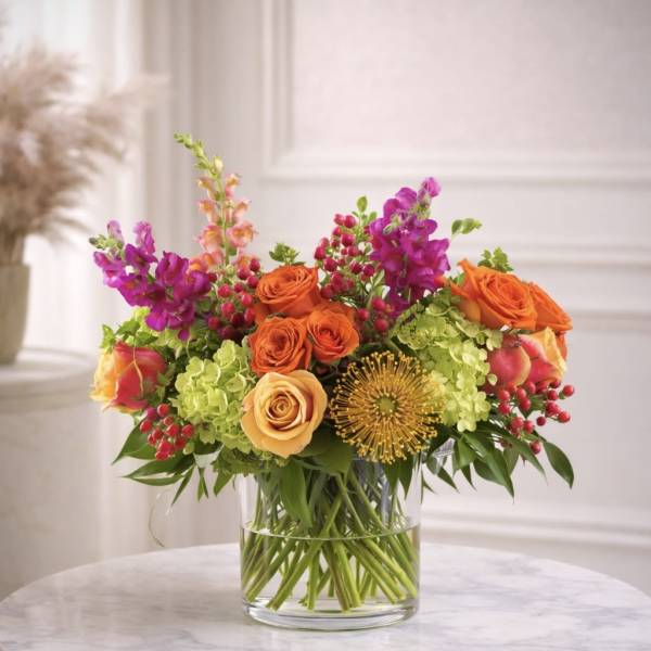 Bright arrangement of orange roses, green hydrangeas, and pink snapdragons in a clear glass vase