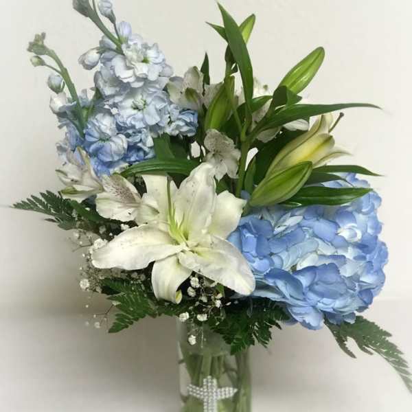 Tall glass vase with blue hydrangeas, white lilies, and other white flowers with a pearl cross on the vase