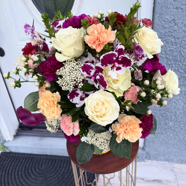 Mixed bouquet of cream roses, orchids, and carnations in a vase