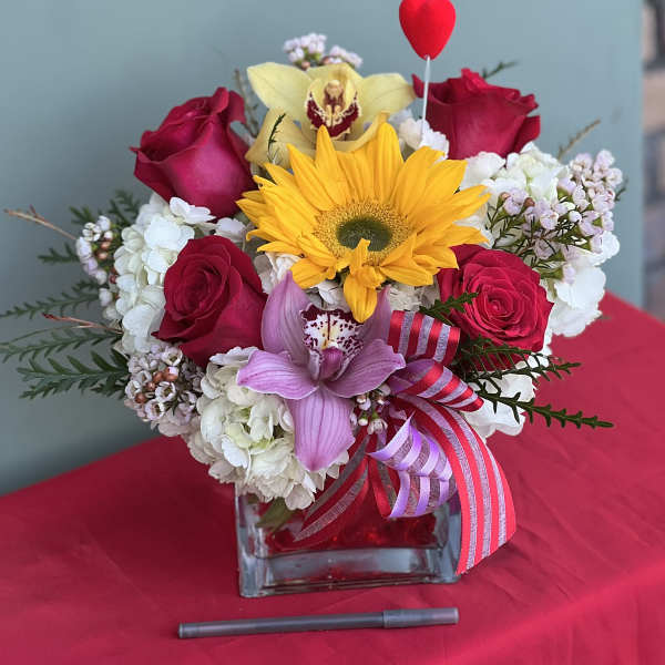 Bouquet of red roses, a yellow sunflower, and pink orchids in a glass vase