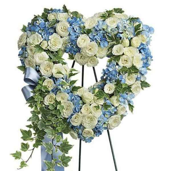 Heart-shaped floral wreath with white roses and blue hydrangeas on an easel