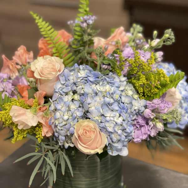 Pastel bouquet with blue hydrangeas, peach roses, and lavender flowers in a glass vase