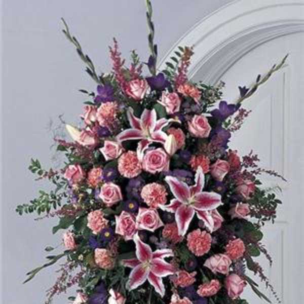 Tall standing floral spray with pink roses and lilies in pink, purple, and white.