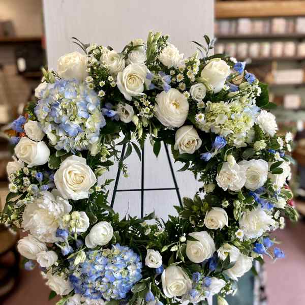 Large white floral wreath with blue accents on a stand