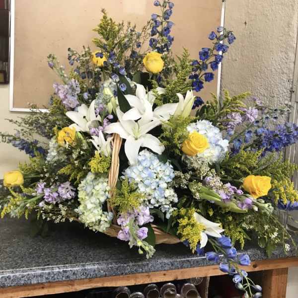 Large basket arrangement with white lilies, yellow roses, blue hydrangeas, and purple flowers