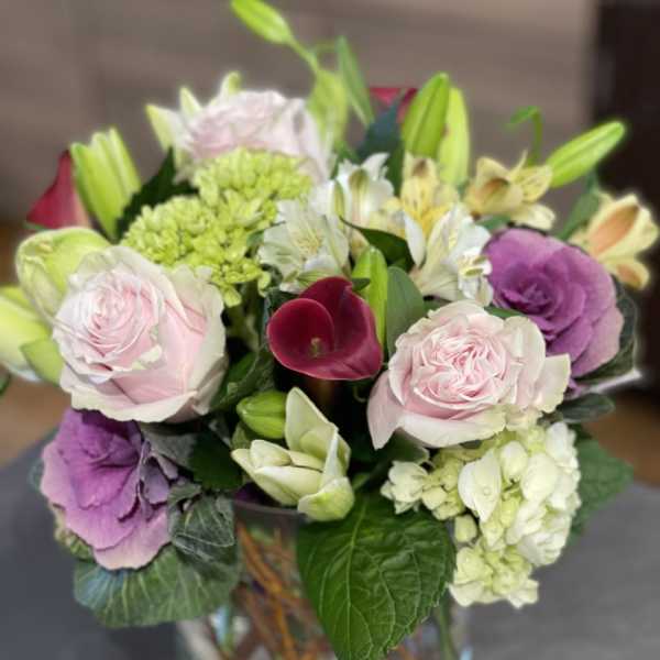 Mixed bouquet with pink roses, lilies, hydrangea, and a burgundy calla lily in a glass vase