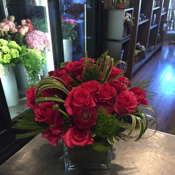 Red rose arrangement in a square glass vase with curled greenery